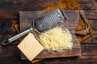 Piece of semi hard cheese and grated cheese with grater. Wooden background. Top view.