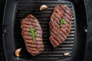 Grilled Top Blade or flat iron roast beef meat steaks on a skillet. Black background. Top View.