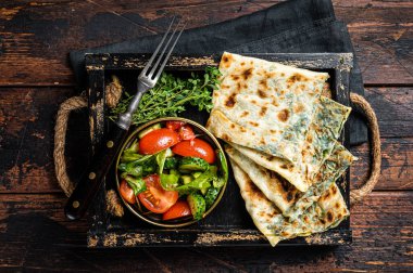 Baked Gozleme flatbread with greens in a box with vegetable salad. Wooden background. Top view.