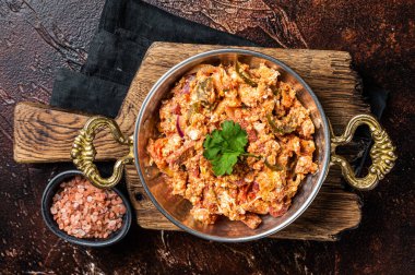 Turkish Menemen omelet with vegetabls and sucuk in askillet. Dark background. Top view.