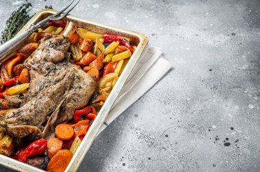 Roast lamb mutton shoulder meat in a baking dish with vegetables. Gray background. Top view. Copy space.