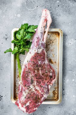 Marinated whole mutton leg, raw lamb meat with thyme, spices and olive oil. Gray background. Top view.