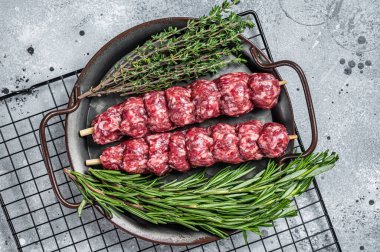Raw Turkish Urfa kebab decorated with herbs, spices and meat fork. Gray background. Top view.