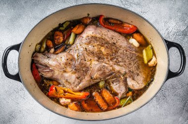 Braised lamb mutton shoulder in a baking dish with vegetables in red wine. White background. Top view.