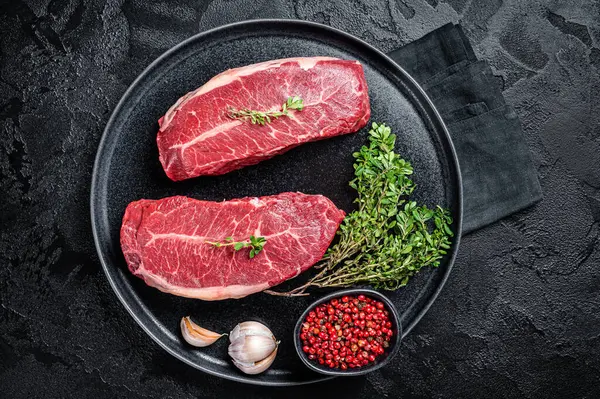 Dry aged Raw top blade flat Iron beef meat steaks. Black background. Top View.