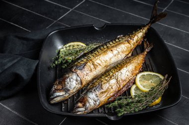 Grilled mackerel fish with lemon, herbs and spices in a skillet. Black background. Top view.