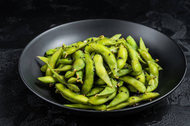 Boiled Edamame Soy Beans with sea salt in a plate. Black background. Top view.