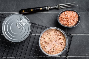 Canned tuna fillet meat in olive oil in a tin. Black background. Top view.