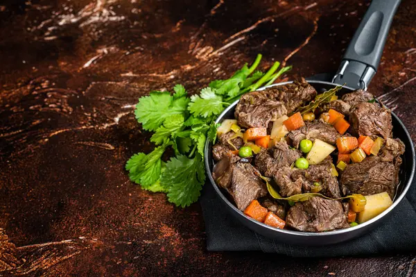 Irish stew with beef meat, potatoes, carrots and herbs in a skillet. Dark background. Top view. Copy space.