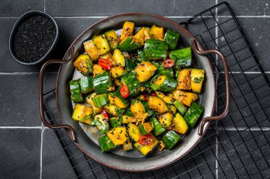Chinese smashed cucumber salad with chili peppers and sesame seeds. Black background. Top view.