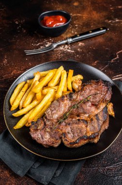 Roasted pork steaks from neck meat in plate with potato chips. Dark background. Top view.