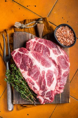 Raw pork steak chops, neck meat with herbs. Orange background. Top view.