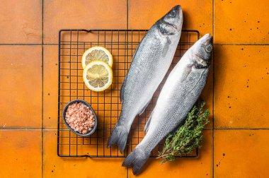 Raw Sea Bass fish with lime and herbs. Orange background. Top view.