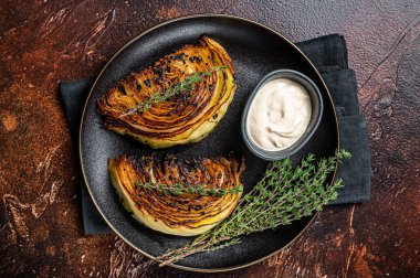 Vegan grilled cabbage steaks with sauce on a black plate. Dark background. Top view.