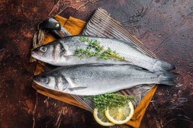 Raw Sea Bass, Branzino fish with thyme and lemon. Dark background. Top view.