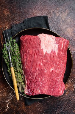 Fresh beef brisket, raw meat with herbs. Dark background. Top view.
