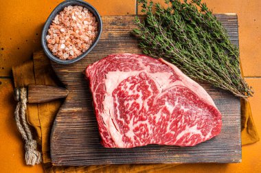 Prime Raw wagyu Rib Eye beef meat steak on wooden board. Orange background. Top view.