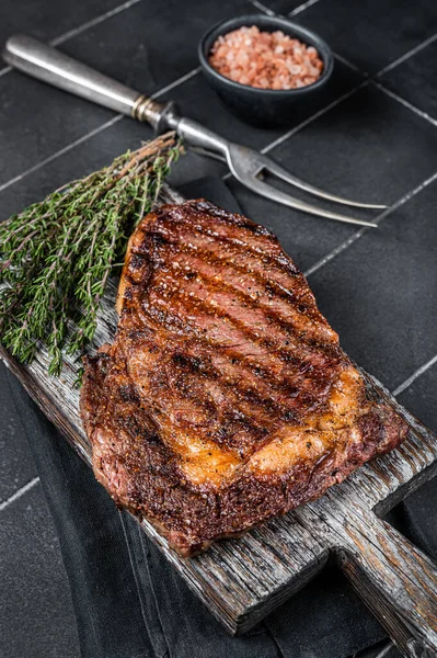 Barbecue aged wagyu Rib Eye beef meat steak with thyme on wooden board. Black background. Top view.