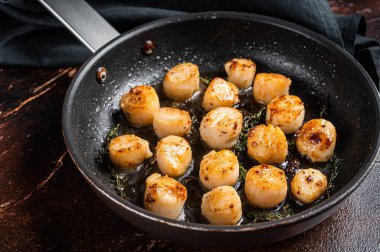 Fried scallops with butter lemon sauce in a skillet. Dark background. Top view.