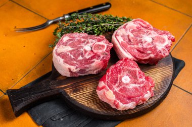 Raw lamb neck chops, fresh mutton meat on a butcher board with herbs. Orange background. Top view.