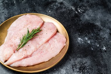 Uncooked Raw chicken chop breast fillets on a plate, poultry meat. Black background. Top view. Copy space.
