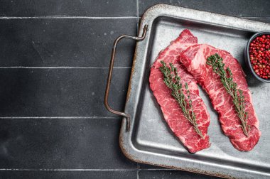 Pişmemiş Denver bifteği, pembe biber ve çelik tepside kekik. Siyah arka plan. Üst Manzara. Boşluğu kopyala.