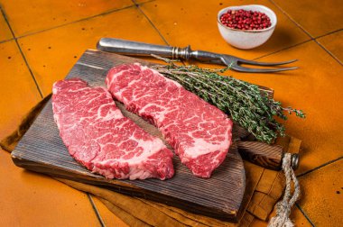 Raw Denver beef meat Steak with pink pepper and thyme. Orange background. Top view.