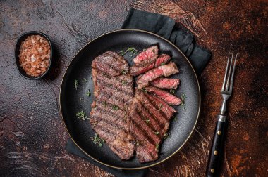 Barbecue denver strip beef meat steak on a plate. Dark background. Top view.