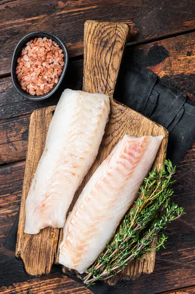 Cod fish fillets, raw codfish with thyme on wooden board. Wooden background. Top view.
