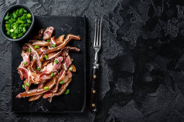 Fried pig ears with sesame seeds and green onions. Fried pork ears in korean style with spicy sauce. Black background. Top view. Copy space.