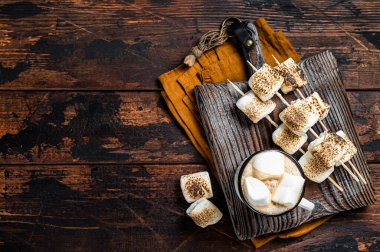 Roasted Marshmallow on the sticks with Cup of coffee on wooden board. Wooden background. Top view. Copy space.