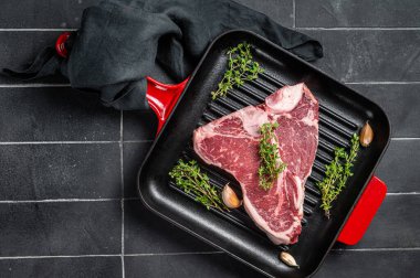 Çiğ T-bone ya da biftekli biftek kekik ile ızgara tavada pişmeye hazır. Siyah arka plan. Üst görünüm.