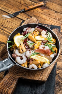 Cooking of fresh seafood mix in a skillet. Wooden background. Top view.