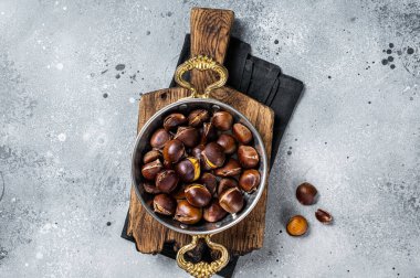 Cracked roasted chestnuts served in a skillet. Gray background. Top view.