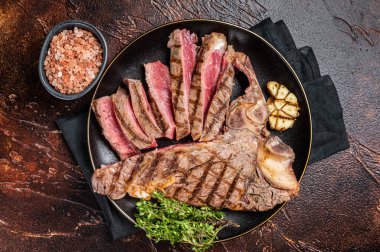 Orta pişmiş ızgara biftek, tabakta dilimlenmiş T-Bone bifteği. Karanlık arka plan. Üst görünüm.