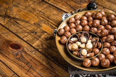 Organic Macadamia nuts in a shell ready to eat. Wooden background. Top view. Copy space.