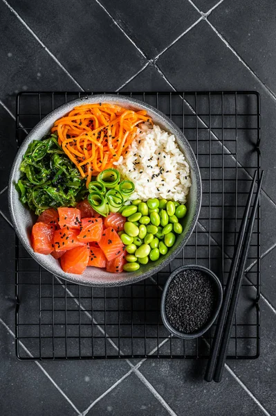 Hawaiian Poke bowl with Salmon, Edamame and Rice. Black background. Top view.