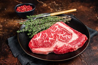 Black Angus Rib Eye steak, raw marbled beef meat with herbs. Dark background. Top view.