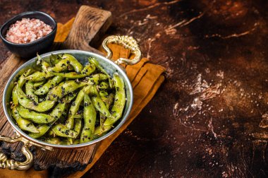 Roasted green Edamame Soy Beans with sea salt and sesame seeds in a skillet. Dark background. Top view. Copy space.