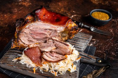 Schweinshaxe Roasted Pork Ham Hock, knuckle with Sauerkraut served on a wooden board. Dark background. Top view.