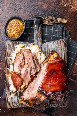 Schweinshaxe Roasted Pork Ham Hock, knuckle with Sauerkraut served on a wooden board. Dark background. Top view.