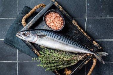 Raw mackerel fish with herbs and spices in wooden tray ready for cooking. Black background. Top view.