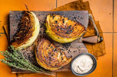 Roasted vegan cabbage steaks with herbs on wooden board. Orange background. Top view.
