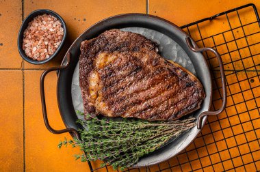 BBQ Grilled wagyu Rib Eye beef meat steak with herbs in steel tray. Orange background. Top view.