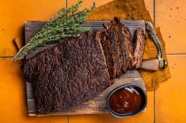 Smoked Barbecue Beef Brisket with Sauce on wooden board. Orange background. Top view.