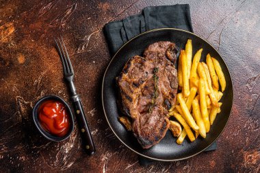 Roasted pork steaks from neck meat in plate with potato chips. Dark background. Top view.