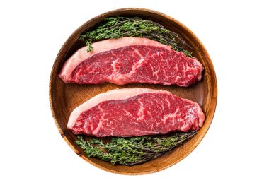 Pişmemiş çiğ sığır filetosu sığır eti bifteği ahşap bir tabakta otlarla birlikte. İzole edilmiş, beyaz arka plan. Üst görünüm