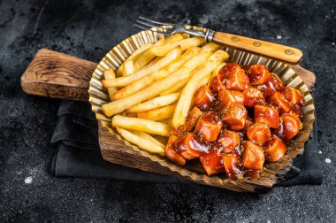 German currywurst with french fry served in a steel plate. Black background. Top view.
