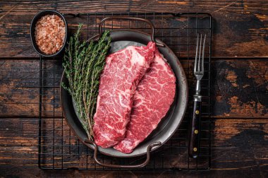 Fresh raw Denver Steak, beef meat with sea salt, seasonings and spices, ready to grill. Wooden background. Top view.