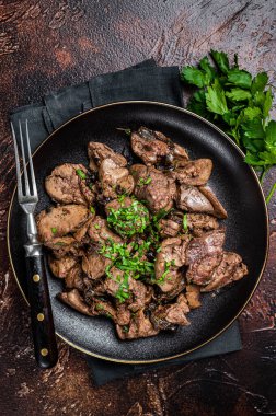 Fried chicken liver with onions and parsley in a plate. Dark background. Top view.